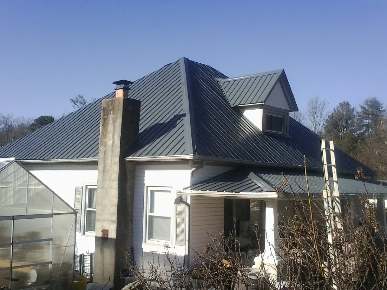 Dark blue standing seam metal roof on a white farmhouse with dormer — Slate & Tile Roof Repair by Roofing Brothers in Robinson