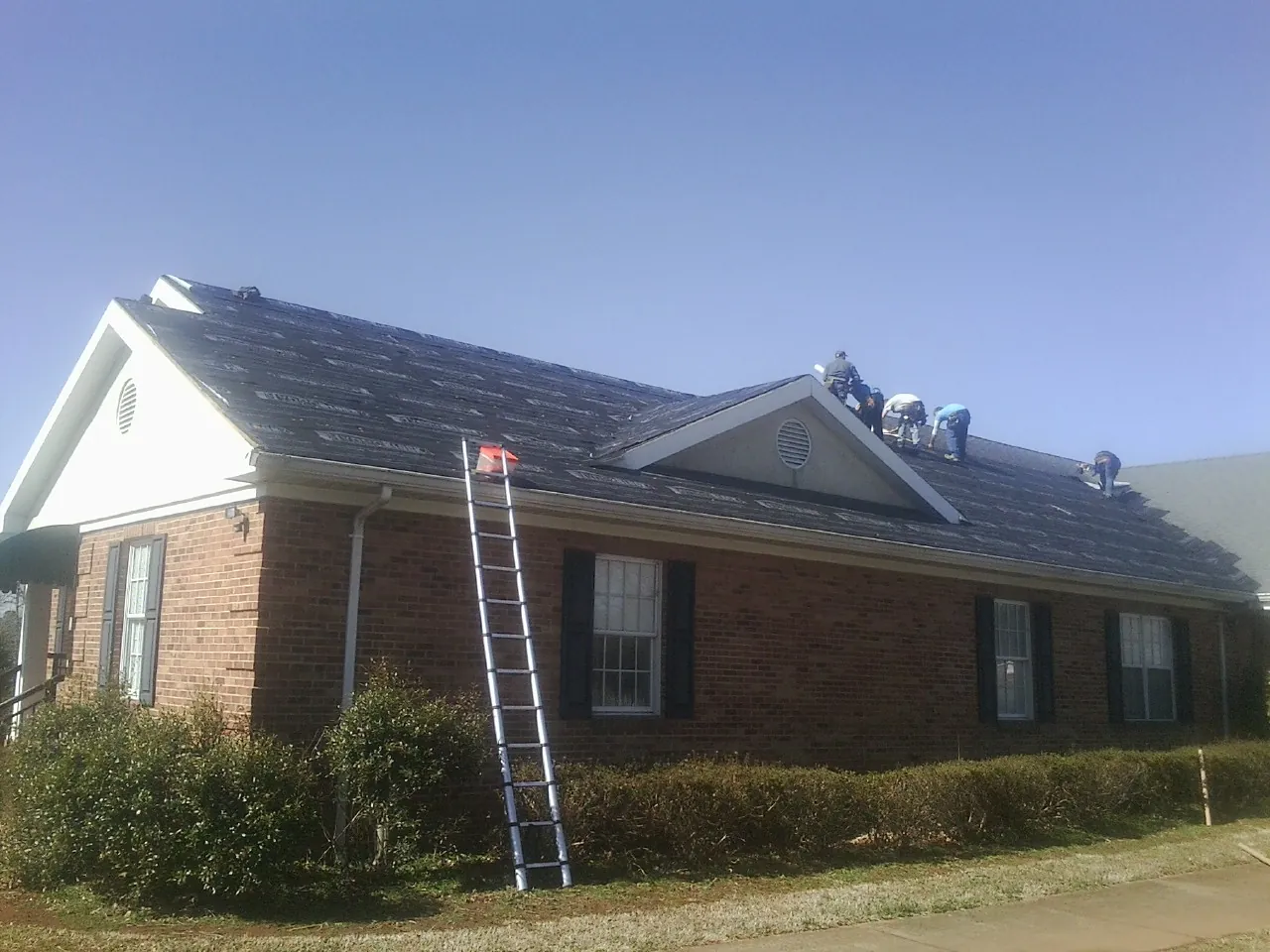 Crew tearing shingles off a brick ranch roof with a ladder set — Metal Roof Repair work by our crew in Robinson