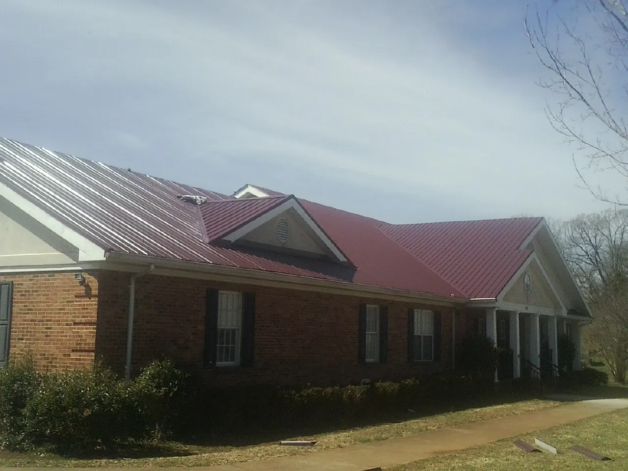 Red metal roof with gabled entries on a long brick building, from a Hail Damage Roof Repair job in Robinson