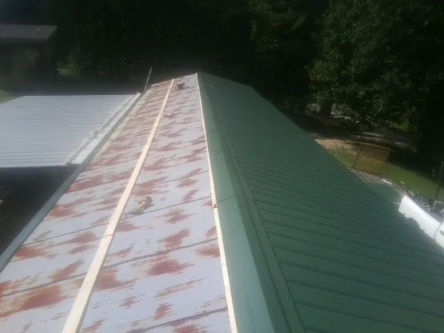 Old rusted panels beside newly installed green metal roofing — Wind Damage Roof Repair by Roofing Brothers in Robinson