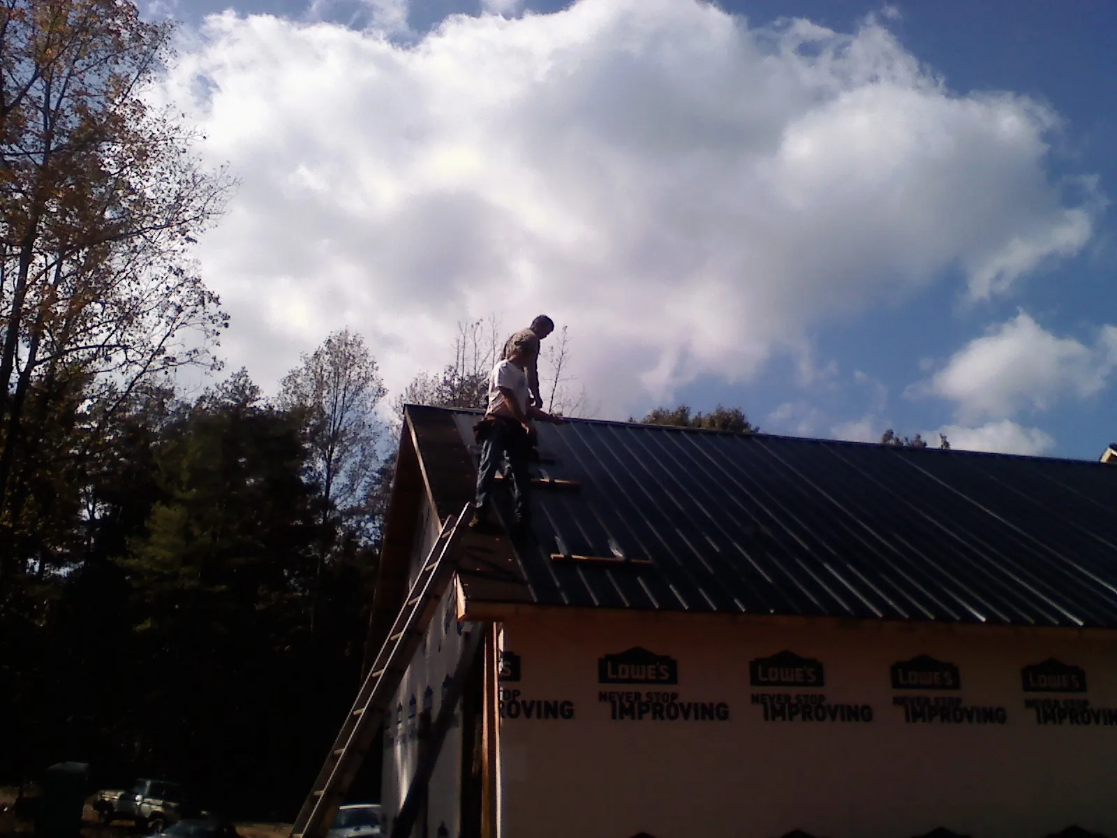 Roofer fastening dark metal panels high against a cloudy sky, from a Roof Inspection job in Robinson